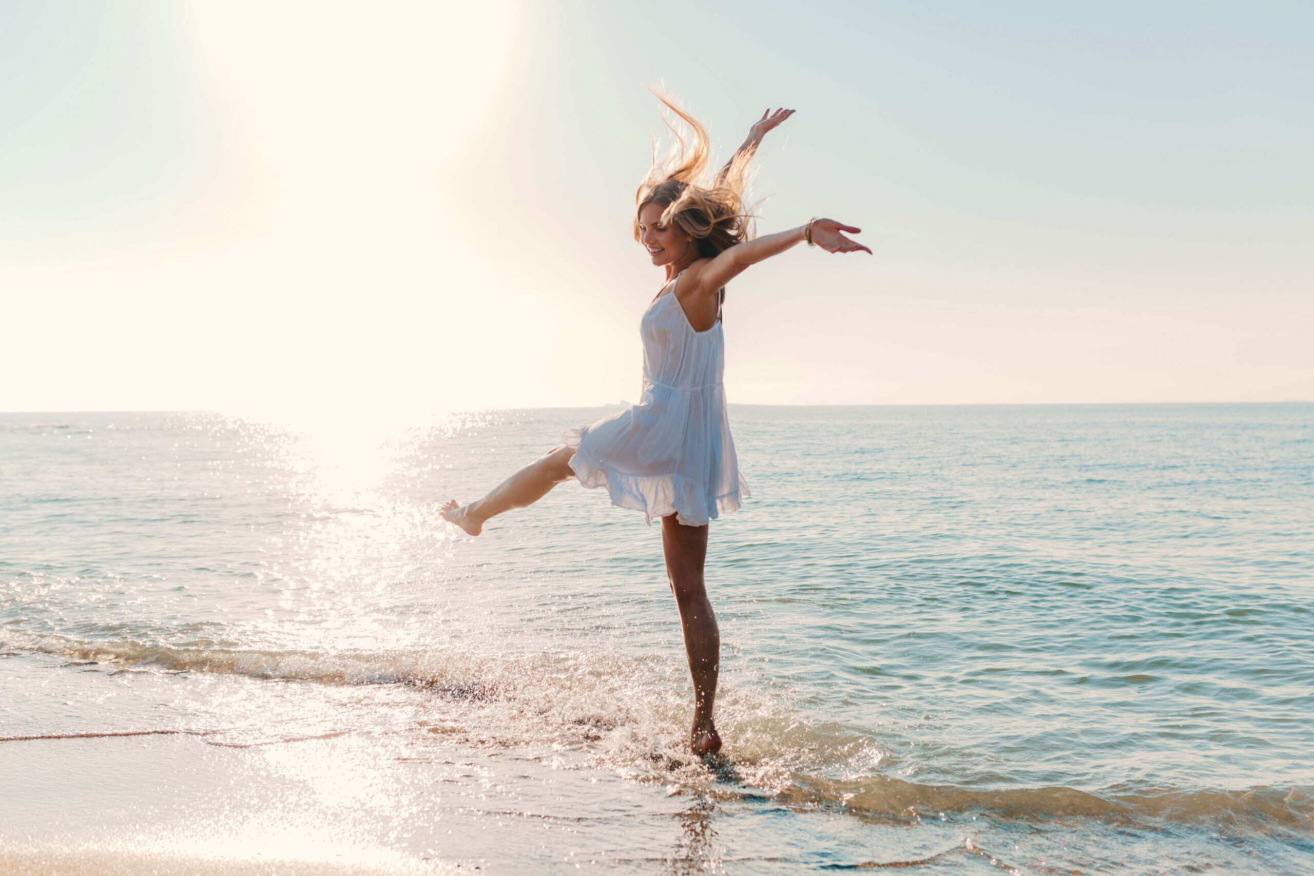 junge attraktive gluckliche frau die durch sonnigen sommermode stil des seestrandes sich dreht